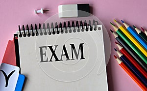 EXAM - a word written in a notebook on a pink background and colored pencils