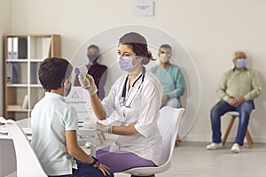 Medical nurse measuring little boy`s temperature using modern non-contact thermometer