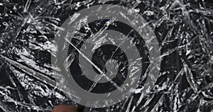 Examine the rotating crumpled polyethylene packaging film through a magnifying glass. The hand raises a magnifying glass