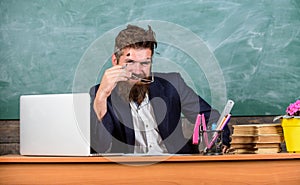 Examiner cunning face sit at table chalkboard background. School exam concept. Examinator bearded teacher with