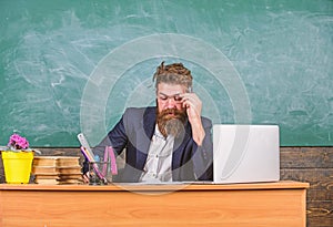 Examiner full of doubts sit at table chalkboard background. School exam concept. Examiner bearded teacher with