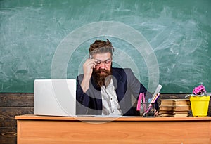 Examiner full of doubts sit at table chalkboard background. School exam concept. Examiner bearded teacher with