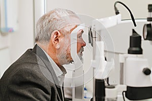 examines elderly man's eye on screen of autorefractometer.