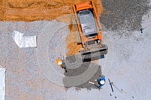 An excavating bucket is in the process of leveling gravel for a building foundation