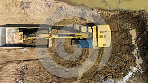 excavating soil into a dump truck to build a pond for store water for use in the dry season for agriculture, aerial top view