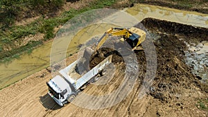 excavating soil into a dump truck to build a pond for store water for use in the dry season for agriculture, aerial top view