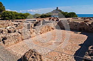 Excavations in Nora, Sardinia - old stone mosaic with remnants of walls and in the background a hill with a watchtower