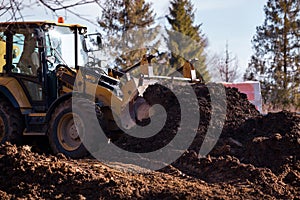 The excavator backfills the pit with the front bucket and moves soil around the construction site. Close-up. Heavy