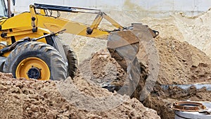 The excavator backfills the pit with the front bucket. Moves soil around the construction site. Close-up. Heavy construction