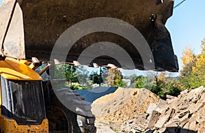 Excavator bucket on blurred background of construction site with pile of sand and old stone blocks