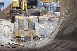 Excavator bucket close-up against the blue sky digs the ground. Earthworks with heavy equipment at the construction site