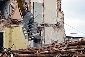 The excavator bucket dismantles the old house and disassembles the damaged beams of the floors