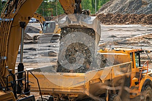 Excavator bucket - loading soil to dump truck, close up photo