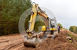 Excavator during construction new road in forest area. Yellow backhoe at groundwork. Earth-moving equipment fort road work,