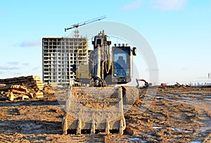Excavator at a construction site on a background of a construction cranes and building. Backhoe dig the ground for the foundation