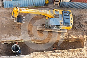 Excavator at a construction site while digging trenches for calcining sewer and drainpipes with a raised bucket, top aerial view