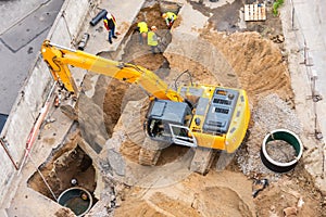 Excavator at a construction site while digging trenches for calcining sewer and drainpipes with a raised bucket, top aerial view