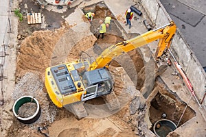 Excavator at a construction site while digging trenches for calcining sewer and drainpipes with a raised bucket, top aerial view