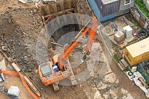 Excavator at a construction site while digging trenches for calcining sewer and drainpipes with a raised bucket, top aerial view