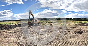 Excavator, construction site, level, against the background of a blue sunny sky and green trees, close-up