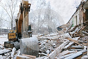 Excavator demolition log wooden house in snowfall