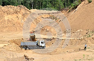 Excavator developing the sand on the opencast and loading it to the heavy dump truck. Processing of loose material in mining