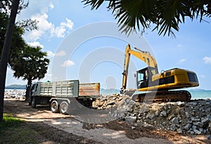 Excavator digger stone and Dump truck working on construction site / backhoe loader on the beach sea ocean