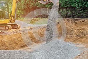 Excavator digging bucket scooping gravel from a building foundation