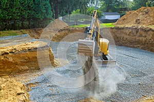 Excavator digging bucket scooping gravel from a building foundation
