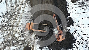 The excavator digs a pit and loads the soil into a dump truck. Drone video.