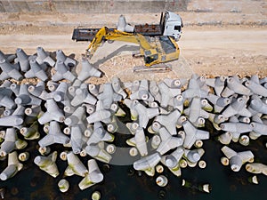 An excavator diligently constructs a dock or breakwater in the sea, its mighty arm reaching out from the shore, creating