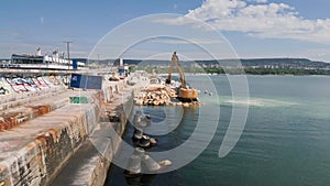 An excavator diligently constructs a dock or breakwater in the sea, its mighty arm reaching out from the shore, creating