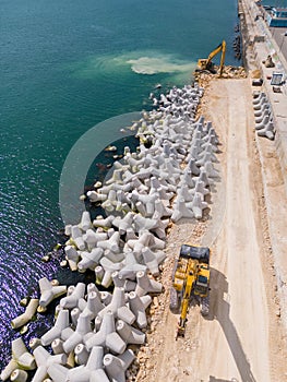 An excavator diligently constructs a dock or breakwater in the sea, its mighty arm reaching out from the shore, creating