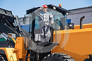 Excavator driver in hard hat stands at construction equipment, concept industrial man portrait