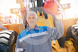 Excavator driver in hard hat stands at construction equipment, concept industrial man portrait