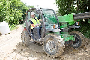 Excavator driver man operator with metal tracks unloading soil at construction