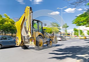 The excavator drives or goes fast on the street with heavy traffic with blue sky and green trees in background, Ankara, Turkey