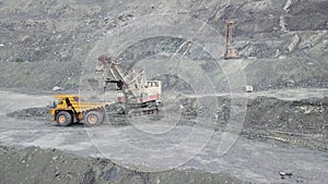 Excavator and dump truck while loading stone ore in a grey quarry, mining industry. Stock. Heavy mining excavator loads