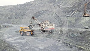 Excavator and dump truck while loading stone ore in a grey quarry, mining industry. Stock. Heavy mining excavator loads