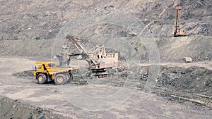 Excavator and dump truck while loading stone ore in a grey quarry, mining industry. Stock. Heavy mining excavator loads