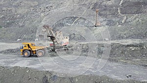 Excavator and dump truck while loading stone ore in a grey quarry, mining industry. Stock. Heavy mining excavator loads