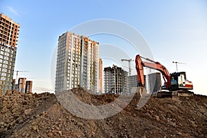 Excavator on earthmoving at construction site. Road work and Dig pit foundation. Tower cranes in action on sunset background.