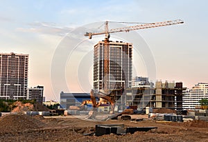 Excavator on earthmoving at construction site. Road work and Dig pit foundation. Tower cranes in action on sunset background.