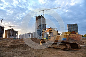 Excavator during earthmoving at construction site on sunset background. Backhoe digs ground for underground sewage and water pipes