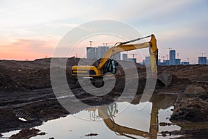 Excavator during earthmoving at construction site on sunset background. Ð¡onstruction machinery for excavating. Small roughness