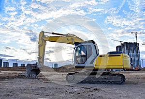 Excavator during earthmoving at construction site on sunset background. Ð¡onstruction machinery for excavating. Tower cranes