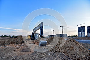 Excavator during earthmoving at construction site on sunset background. Ð¡onstruction machinery for excavating. Tower cranes