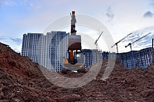 Excavator during earthmoving at construction site on sunset background. Ð¡onstruction machinery for excavating. Tower cranes