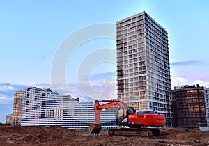 Excavator during earthmoving at construction site on sunset background. Ð¡onstruction machinery for excavating. Tower cranes