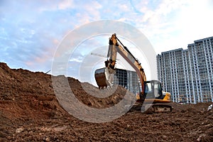 Excavator during earthmoving at construction site on sunset background. Ð¡onstruction machinery for excavating. Tower cranes